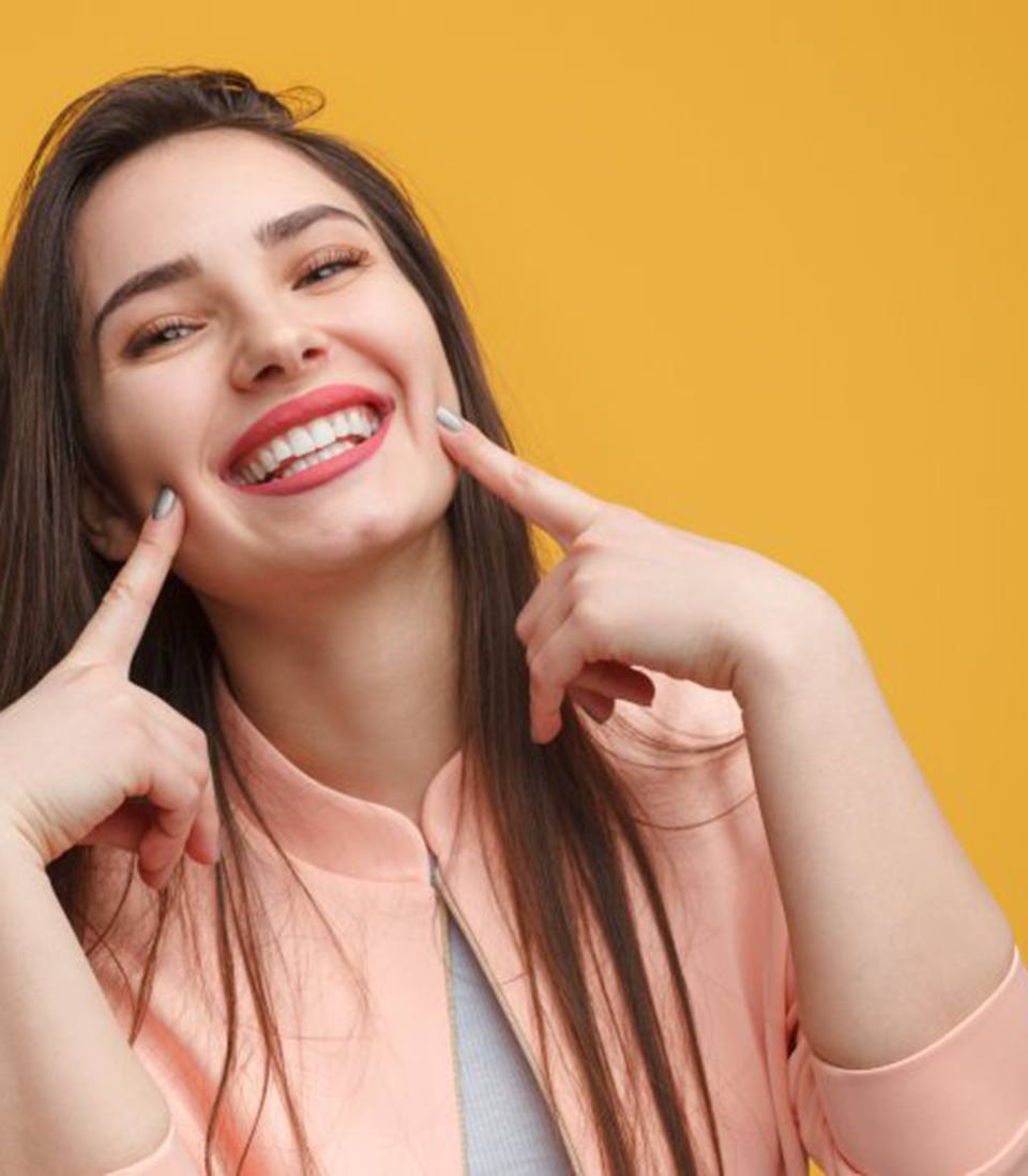 Woman smiling brightly and pointing at her dental bonding results