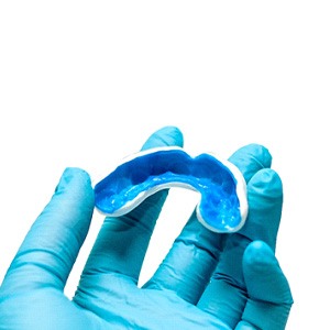Dentist with blue glove holding white and blue mouthguard